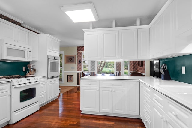 kitchen with a peninsula, white appliances, dark wood-style flooring, and white cabinetry