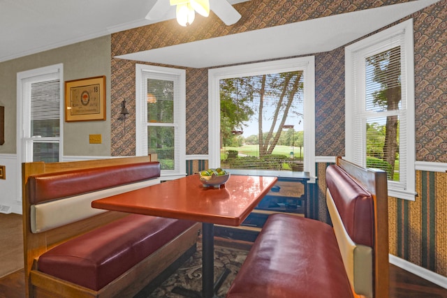 dining area featuring ornamental molding, a ceiling fan, a wainscoted wall, and wallpapered walls