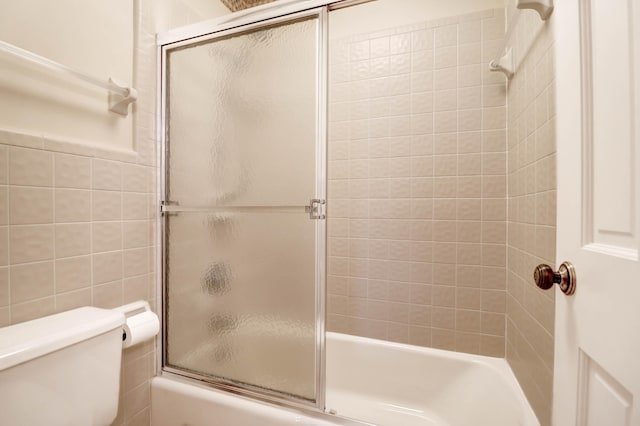 full bath with toilet, bath / shower combo with glass door, and tile walls