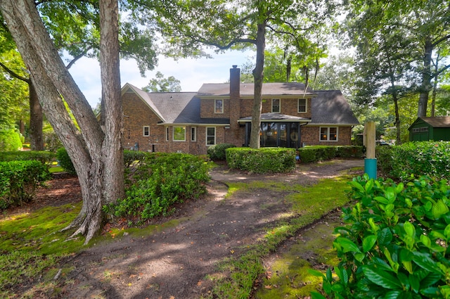 rear view of property featuring a sunroom, a chimney, and brick siding