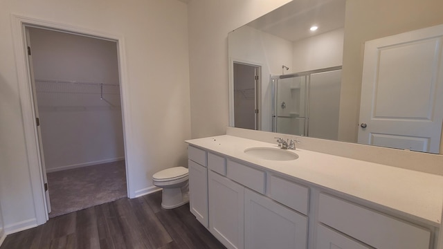 bathroom with wood finished floors, a shower stall, vanity, a spacious closet, and toilet