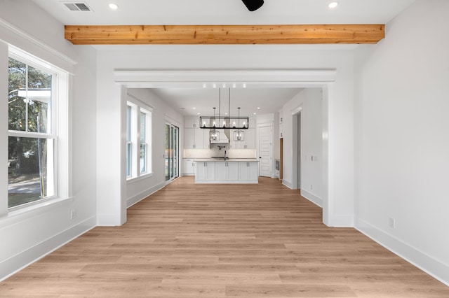 unfurnished living room featuring sink, beamed ceiling, and light wood-type flooring