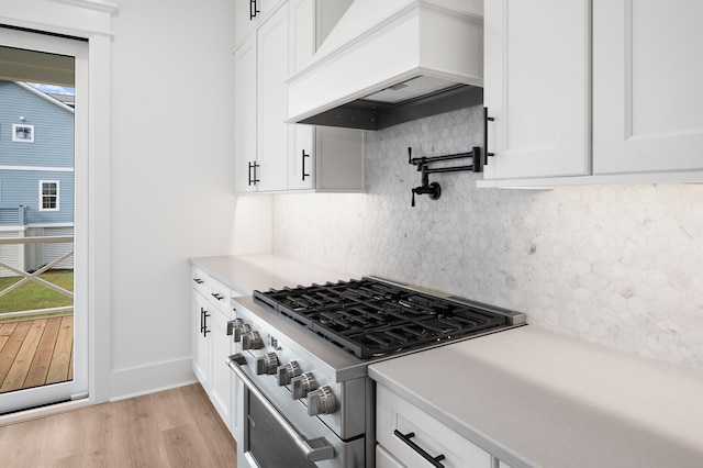 kitchen featuring white cabinetry, high end stove, backsplash, custom exhaust hood, and light wood-type flooring