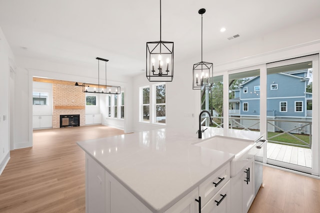 kitchen with hanging light fixtures, an island with sink, sink, and white cabinets