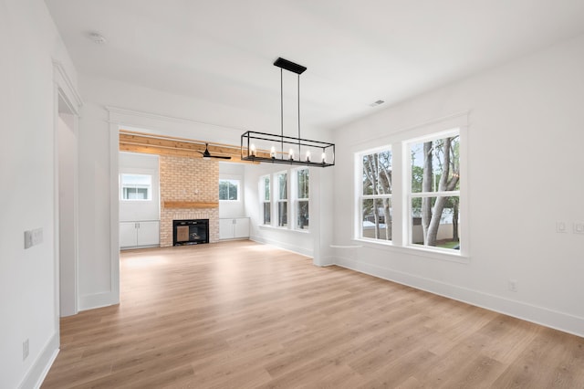 unfurnished living room featuring a brick fireplace, a notable chandelier, and light hardwood / wood-style flooring