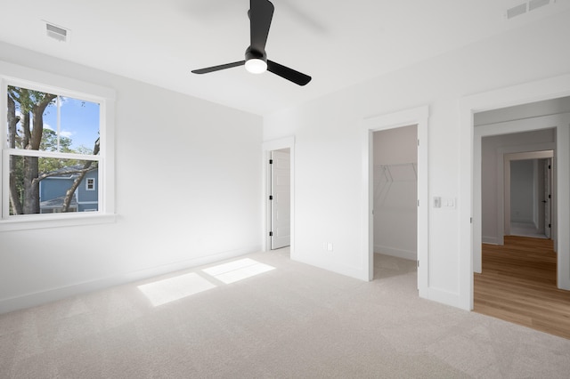 unfurnished bedroom featuring a walk in closet, light colored carpet, a closet, and ceiling fan