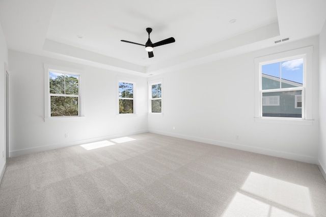 unfurnished room featuring ceiling fan, light colored carpet, and a raised ceiling