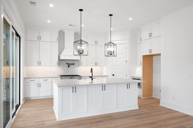 kitchen featuring light wood-type flooring, white cabinetry, premium range hood, and a kitchen island with sink