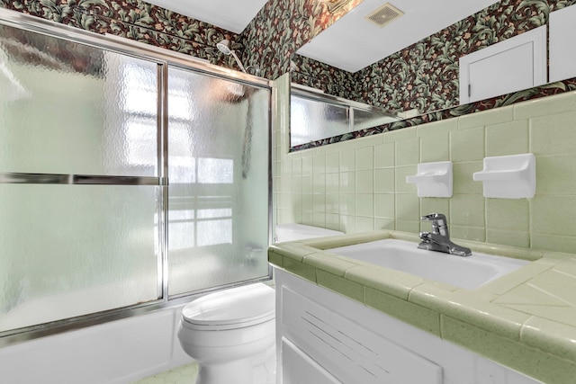 bathroom featuring visible vents, toilet, combined bath / shower with glass door, tile walls, and wallpapered walls