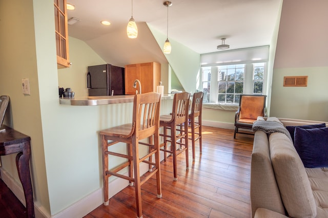 kitchen with pendant lighting, a breakfast bar area, black fridge, vaulted ceiling, and hardwood / wood-style flooring