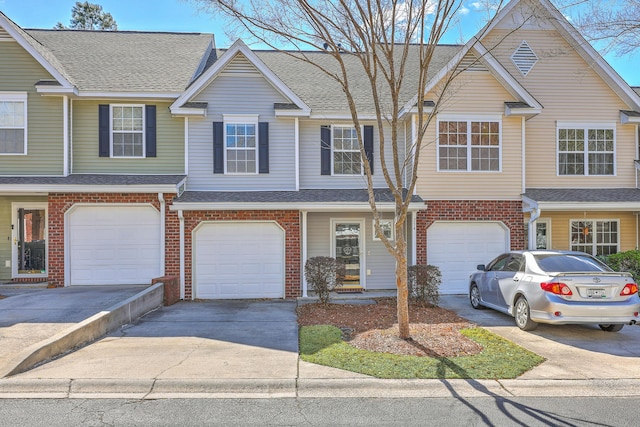 townhome / multi-family property featuring brick siding, driveway, an attached garage, and roof with shingles