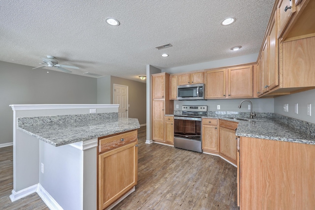 kitchen with visible vents, a sink, a kitchen island, wood finished floors, and appliances with stainless steel finishes