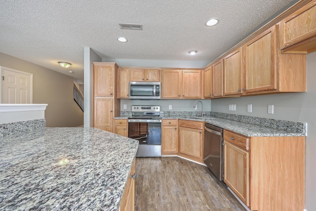 kitchen with visible vents, a sink, wood finished floors, appliances with stainless steel finishes, and light stone countertops