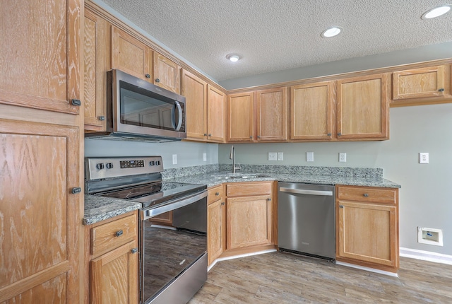 kitchen featuring light stone counters, appliances with stainless steel finishes, light wood-style floors, and a sink