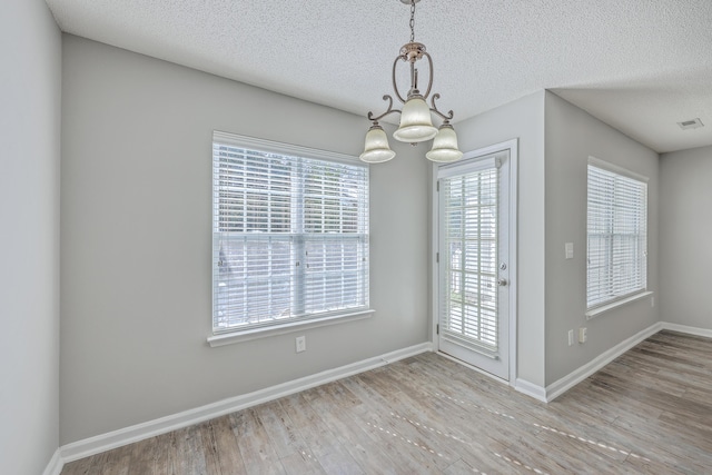 unfurnished dining area featuring wood finished floors, visible vents, baseboards, a textured ceiling, and a chandelier