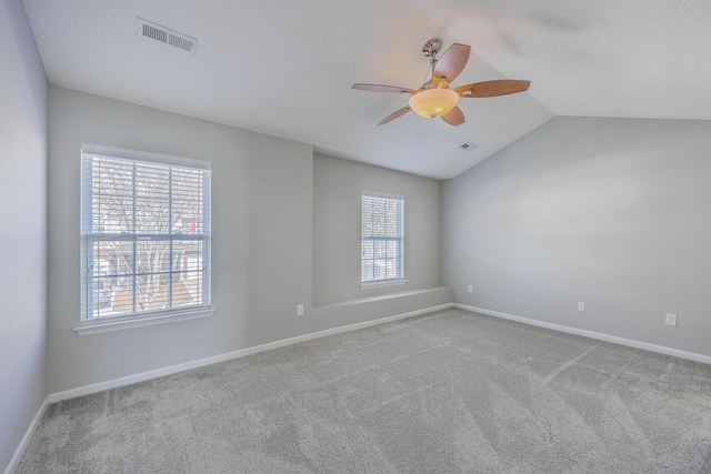 carpeted empty room featuring a wealth of natural light, visible vents, baseboards, and vaulted ceiling