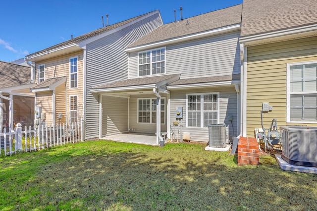 rear view of property featuring fence, roof with shingles, central AC, a yard, and a patio area