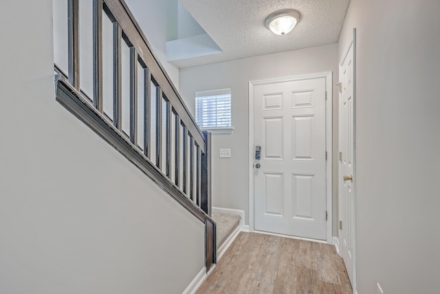 foyer featuring stairs, baseboards, light wood-type flooring, and a textured ceiling