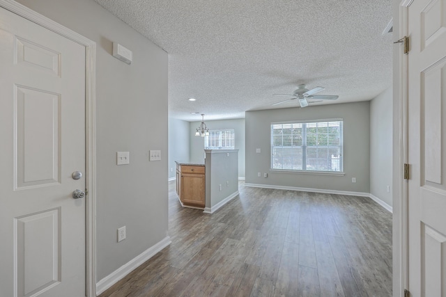 unfurnished living room featuring dark wood-style floors, ceiling fan with notable chandelier, a textured ceiling, and baseboards