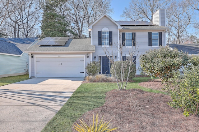 colonial home with solar panels, concrete driveway, a chimney, an attached garage, and a front yard