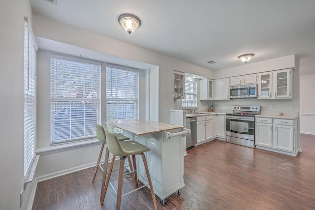 kitchen with dark wood-style floors, light countertops, appliances with stainless steel finishes, and glass insert cabinets