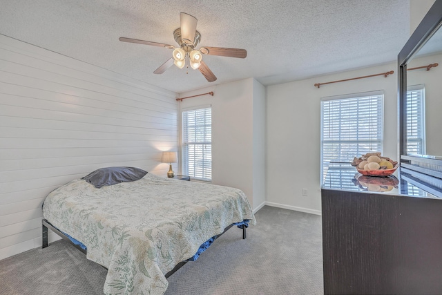 carpeted bedroom with a textured ceiling, baseboards, a ceiling fan, and wooden walls