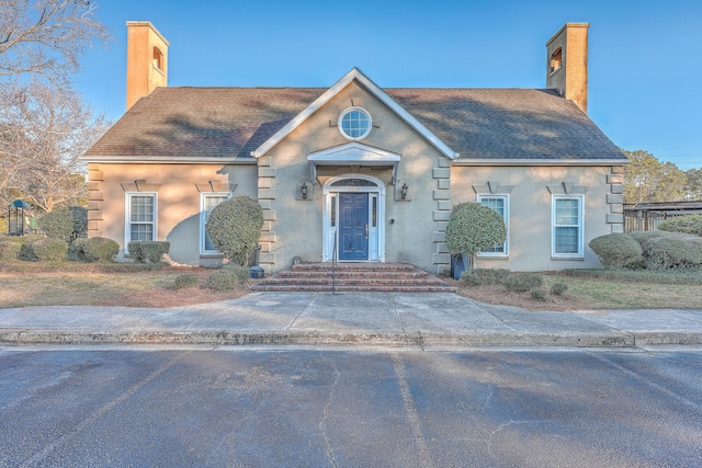 view of front of home featuring a shingled roof, a chimney, and stucco siding