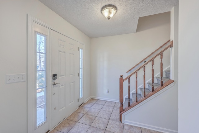 entryway with light tile patterned floors, a textured ceiling, baseboards, and stairs