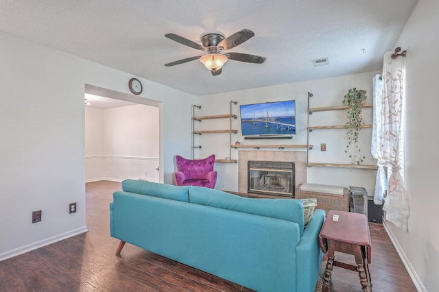 living room with a textured ceiling, ceiling fan, a tile fireplace, and wood finished floors