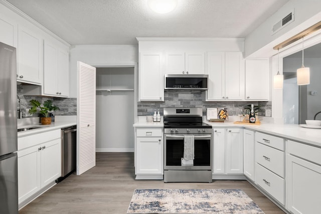 kitchen featuring appliances with stainless steel finishes, backsplash, light countertops, white cabinetry, and a textured ceiling