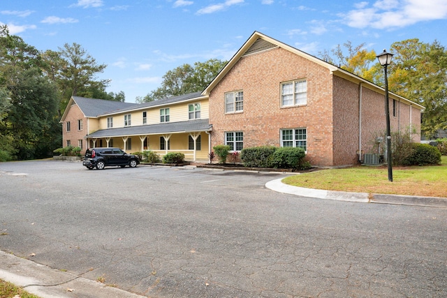 view of front of property featuring covered porch, brick siding, uncovered parking, and cooling unit