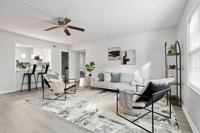 living area featuring light wood-type flooring, ceiling fan, and baseboards