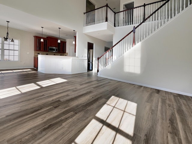 unfurnished living room with a high ceiling, an inviting chandelier, and dark wood-type flooring