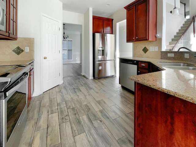 kitchen featuring hanging light fixtures, sink, tasteful backsplash, light stone counters, and stainless steel appliances