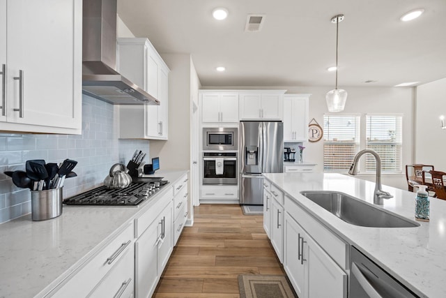 291 Lucca Dr, Summerville, SC 29486 - kitchen with stainless steel appliances, wall chimney range hood, white cabinets, light wood finished floors, and decorative light fixtures