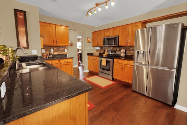 kitchen with appliances with stainless steel finishes, tasteful backsplash, sink, dark stone countertops, and dark wood-type flooring