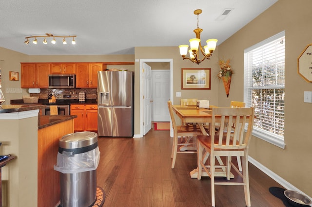 kitchen featuring dark wood-type flooring, appliances with stainless steel finishes, hanging light fixtures, backsplash, and a chandelier