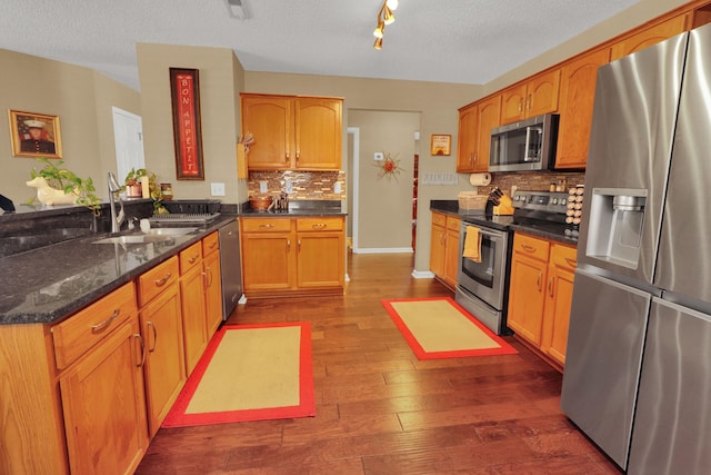 kitchen featuring sink, dark stone counters, dark hardwood / wood-style flooring, stainless steel appliances, and decorative backsplash