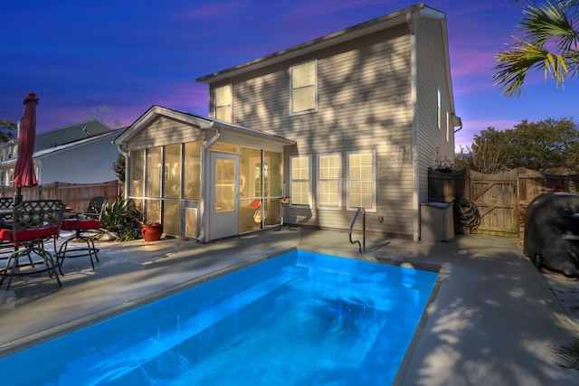 back house at dusk with a fenced in pool, a sunroom, and a patio