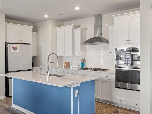 kitchen with white cabinetry, a kitchen island with sink, and wall chimney exhaust hood