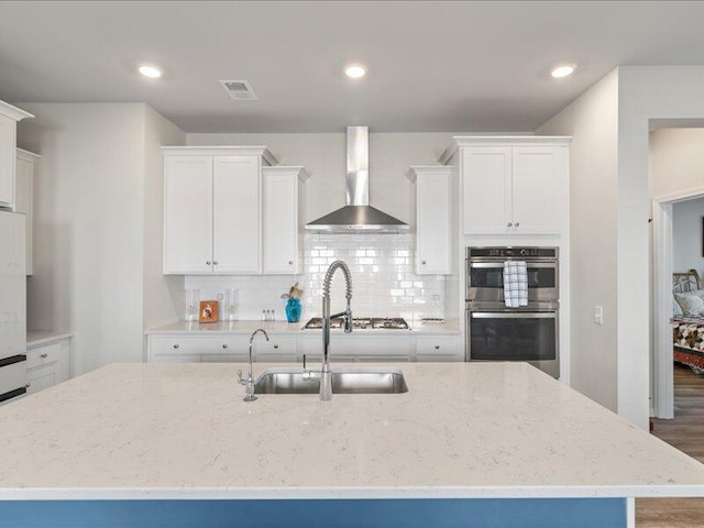 kitchen with white cabinets, wall chimney exhaust hood, and an island with sink