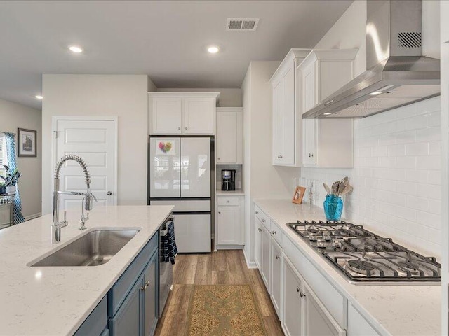 kitchen with white cabinets, wall chimney range hood, sink, and appliances with stainless steel finishes