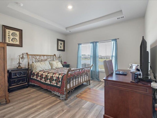 bedroom with a raised ceiling and wood-type flooring