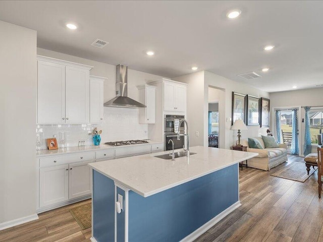 kitchen featuring dark hardwood / wood-style floors, white cabinetry, wall chimney range hood, and a kitchen island with sink