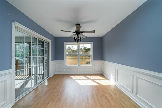 interior space featuring a ceiling fan, light wood-type flooring, and wainscoting