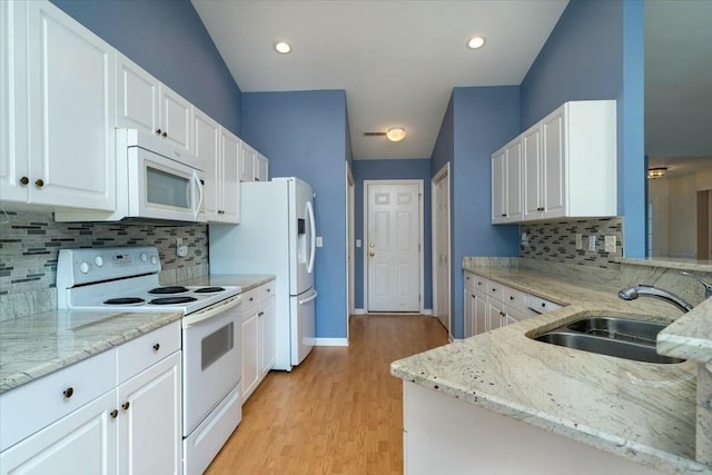 kitchen featuring white appliances, white cabinets, light wood-style flooring, light stone counters, and a sink