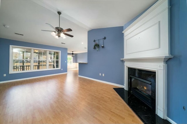 unfurnished living room featuring a high end fireplace, vaulted ceiling, ceiling fan, wood finished floors, and baseboards