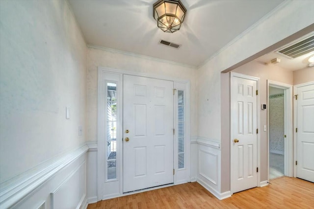 entryway featuring a wainscoted wall, visible vents, crown molding, and light wood finished floors