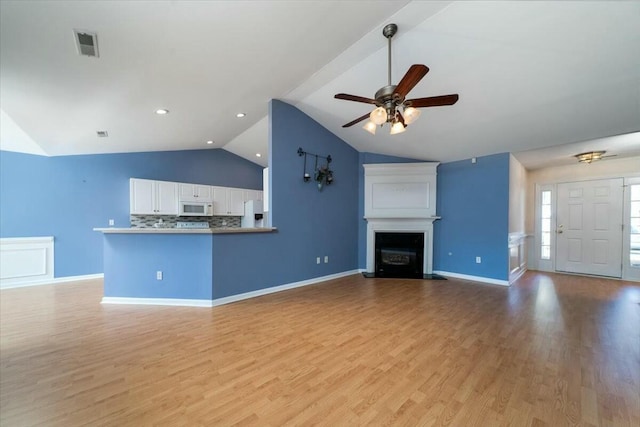 unfurnished living room with a ceiling fan, visible vents, vaulted ceiling, light wood-style floors, and a glass covered fireplace