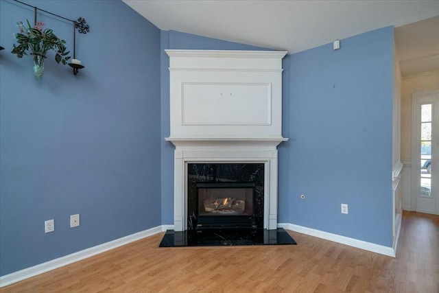 unfurnished living room with wood finished floors, vaulted ceiling, baseboards, and a premium fireplace